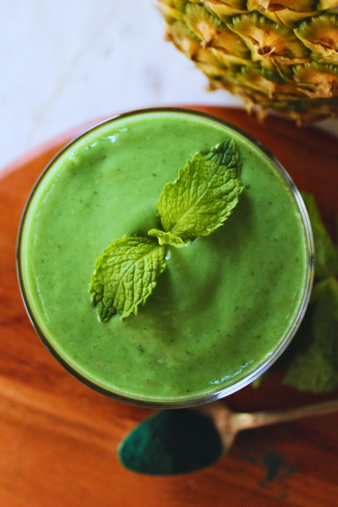 overhead image of a refreshing green smoothie with spirulina powder and topped with fresh mint