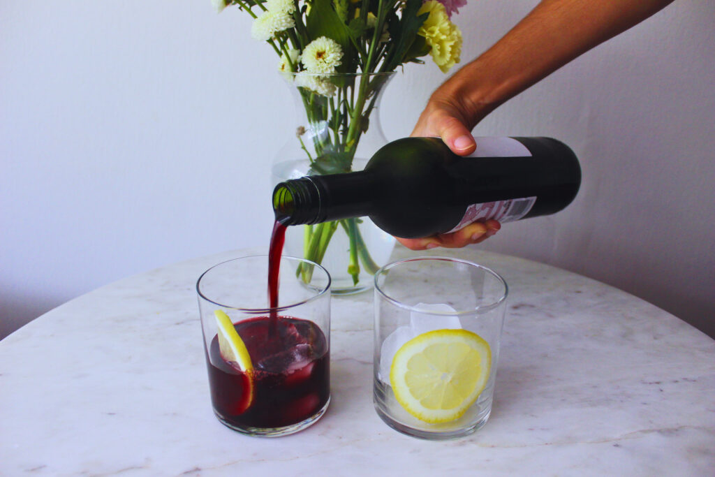 Image of wine being poured into two clear glasses with lemon wheel 