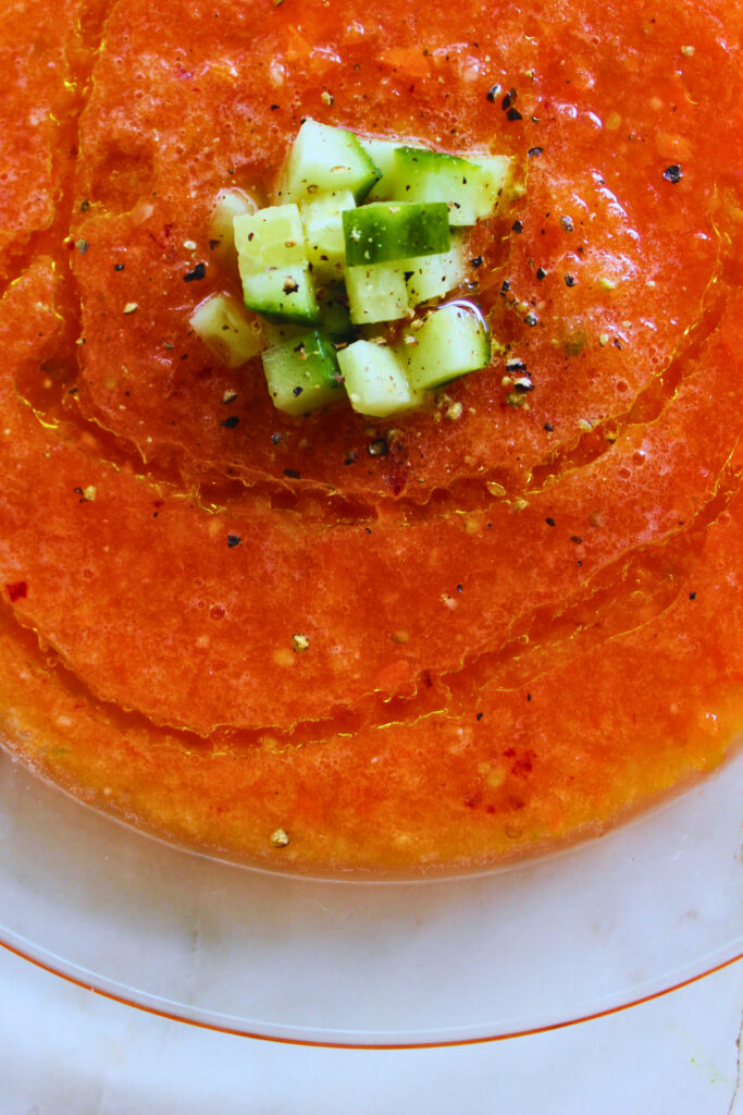 close up of gazpacho topped with fresh cucumber, black pepper and olive oil drizzle