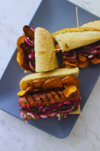 image of a plate fo sandwiches with vegan sausage or tempeh, sliced sweet potato and salsa criolla