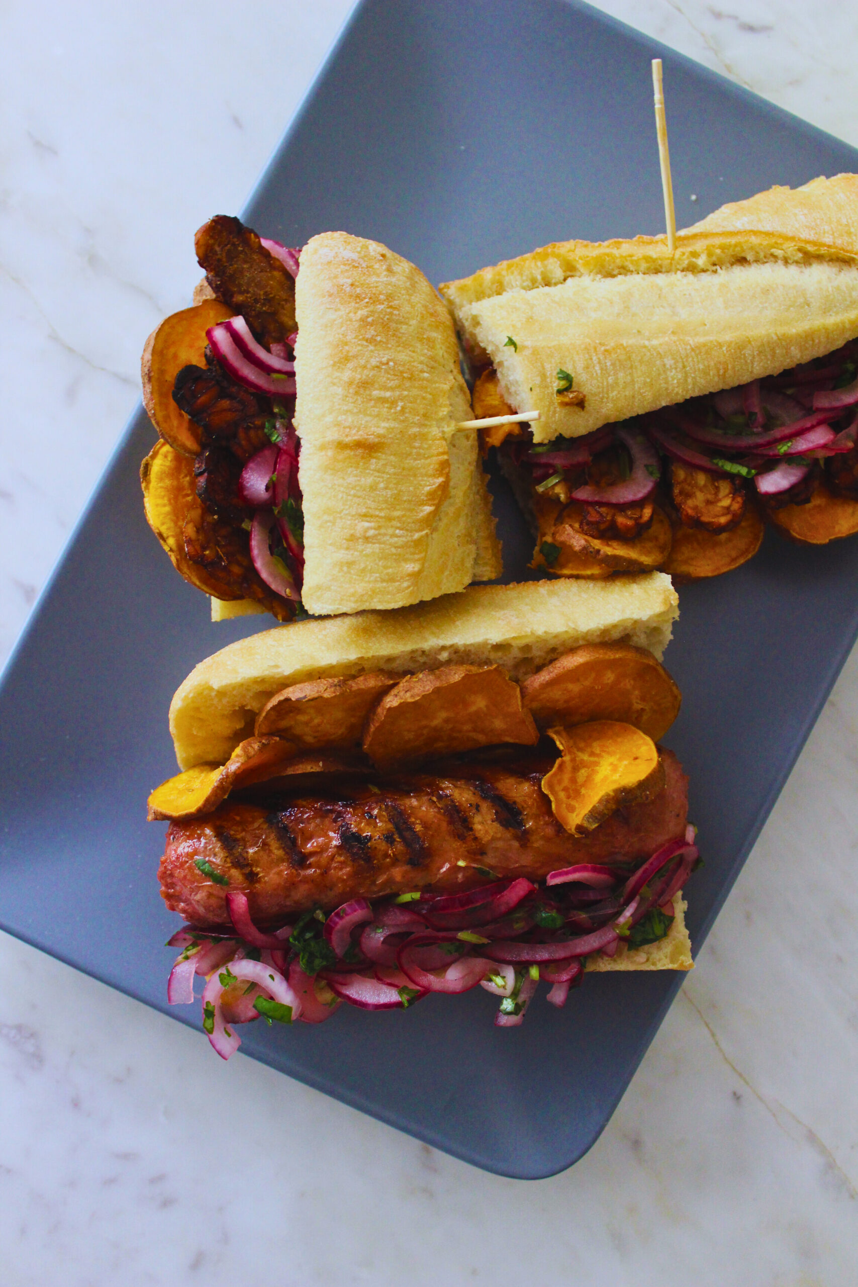 image of a plate fo sandwiches with vegan sausage or tempeh, sliced sweet potato and salsa criolla