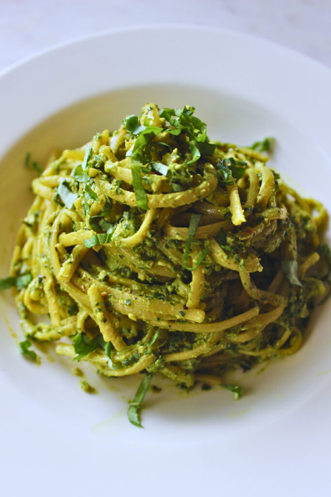 vegan Peruvian tallarines verde. Peruvian pesto served on a white plate topped with fresh basil