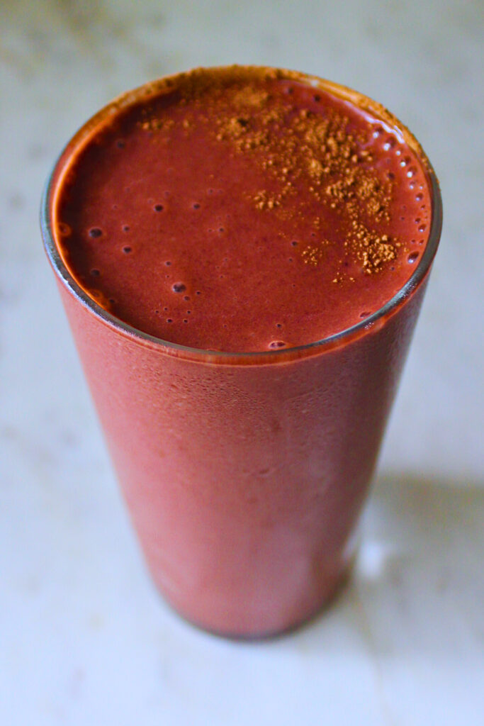 image of a cold glass of red velvet smoothie garnished with a sprinkle of cocoa powder