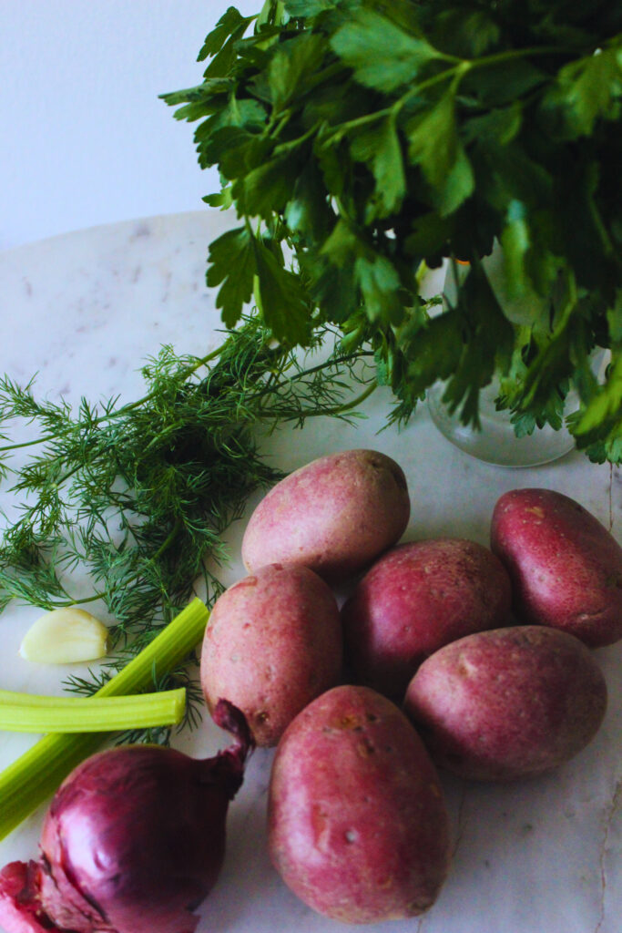image of fresh parsley, fresh dill, whole red potatoes, fresh garlic clove, celery sticks and a red onion.