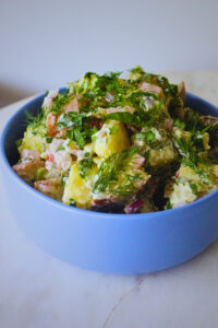 image of freshly prepared herby potato salad in a light blue bowl on a marble top bistro table