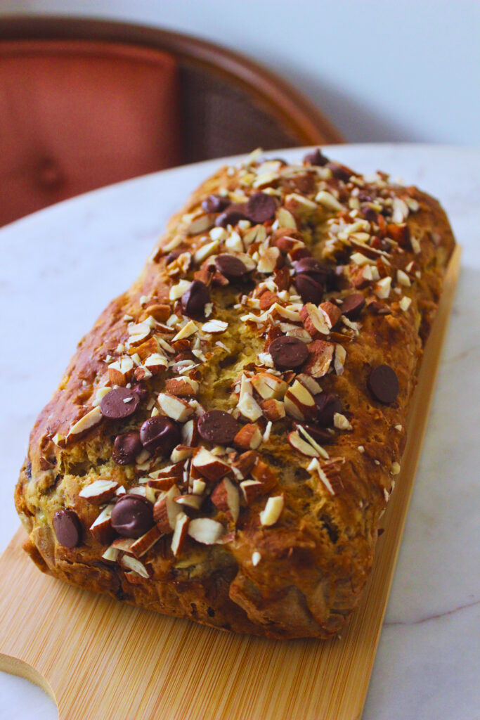 image of banana bread topped with nuts and chocolate on a wooden board