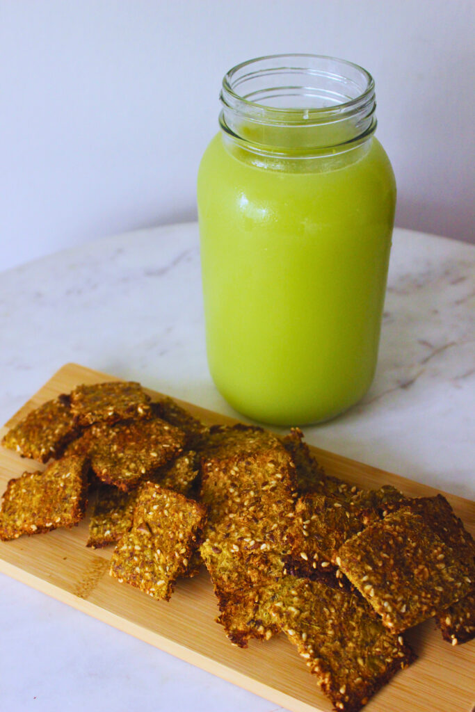 image of celery apple juice in a mason jar beside a wooden board with baked pulp crackers