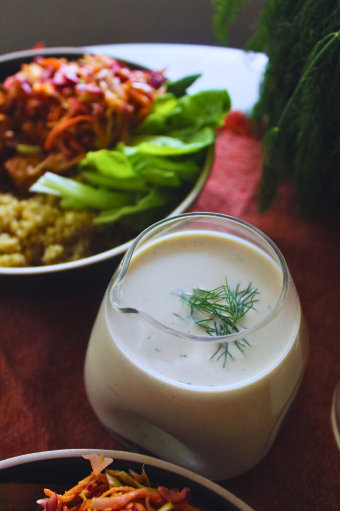 image of a table set up with bowls of food and a glass pitcher of dill pickle dressing