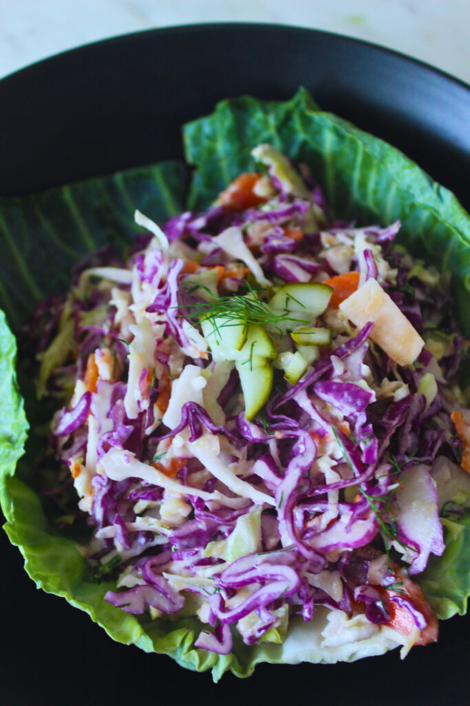 close-up image of dill pickle coleslaw served on a large leaf topped with chopped pickles and fresh dill
