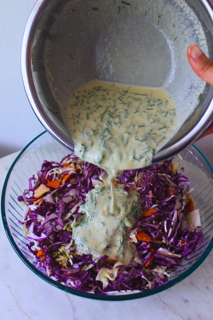 image of dill pickle tahini dressing being poured into a large bowl of shredded cabbage and carrot