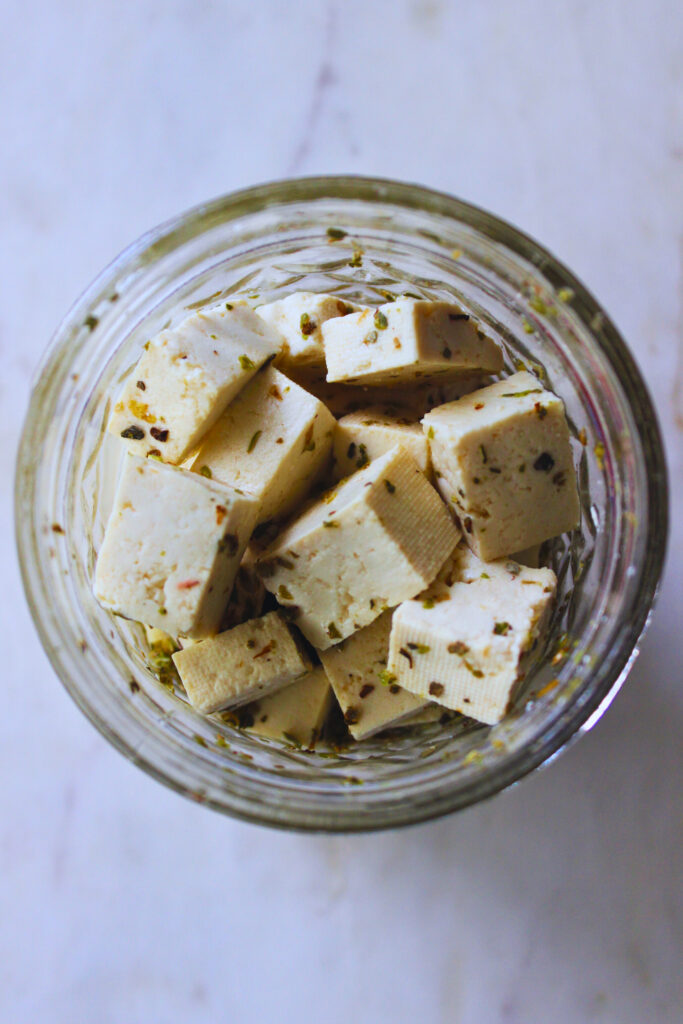 overhead image of tofu feta cut into cubes and seasoned in a glass jar