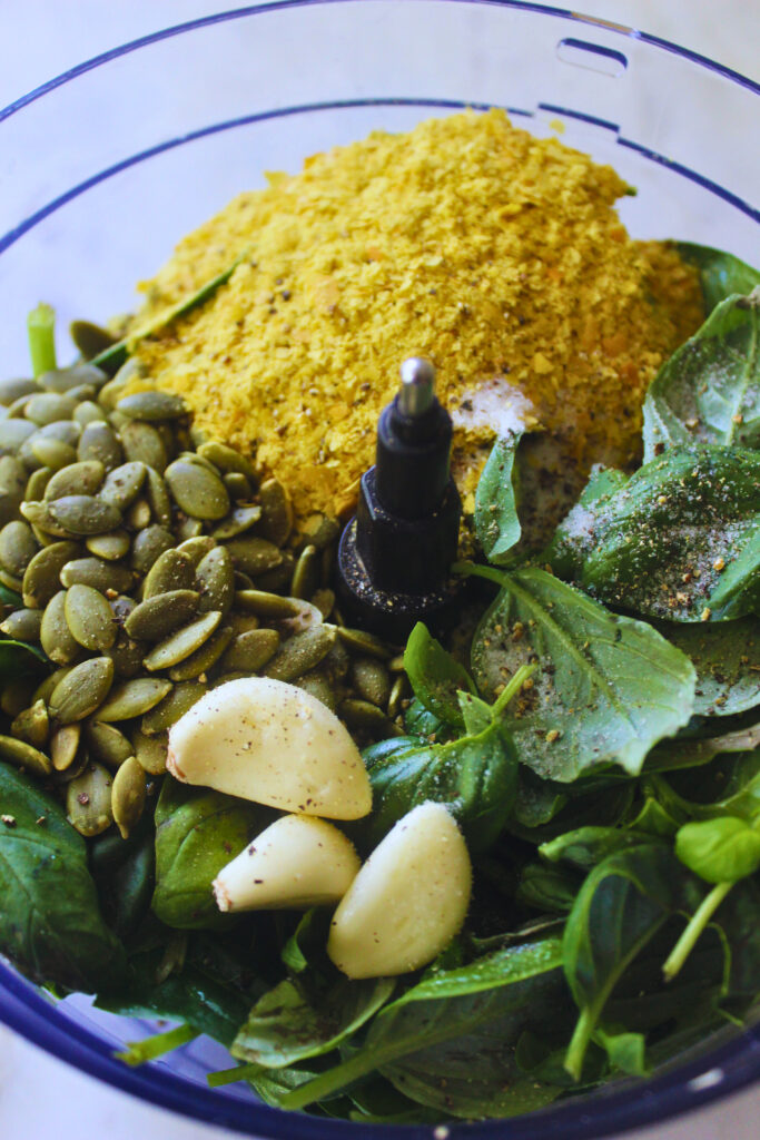 Image of fresh basil, spinach, garlic, pumpkin seeds and nutritional yeast in a food processor
