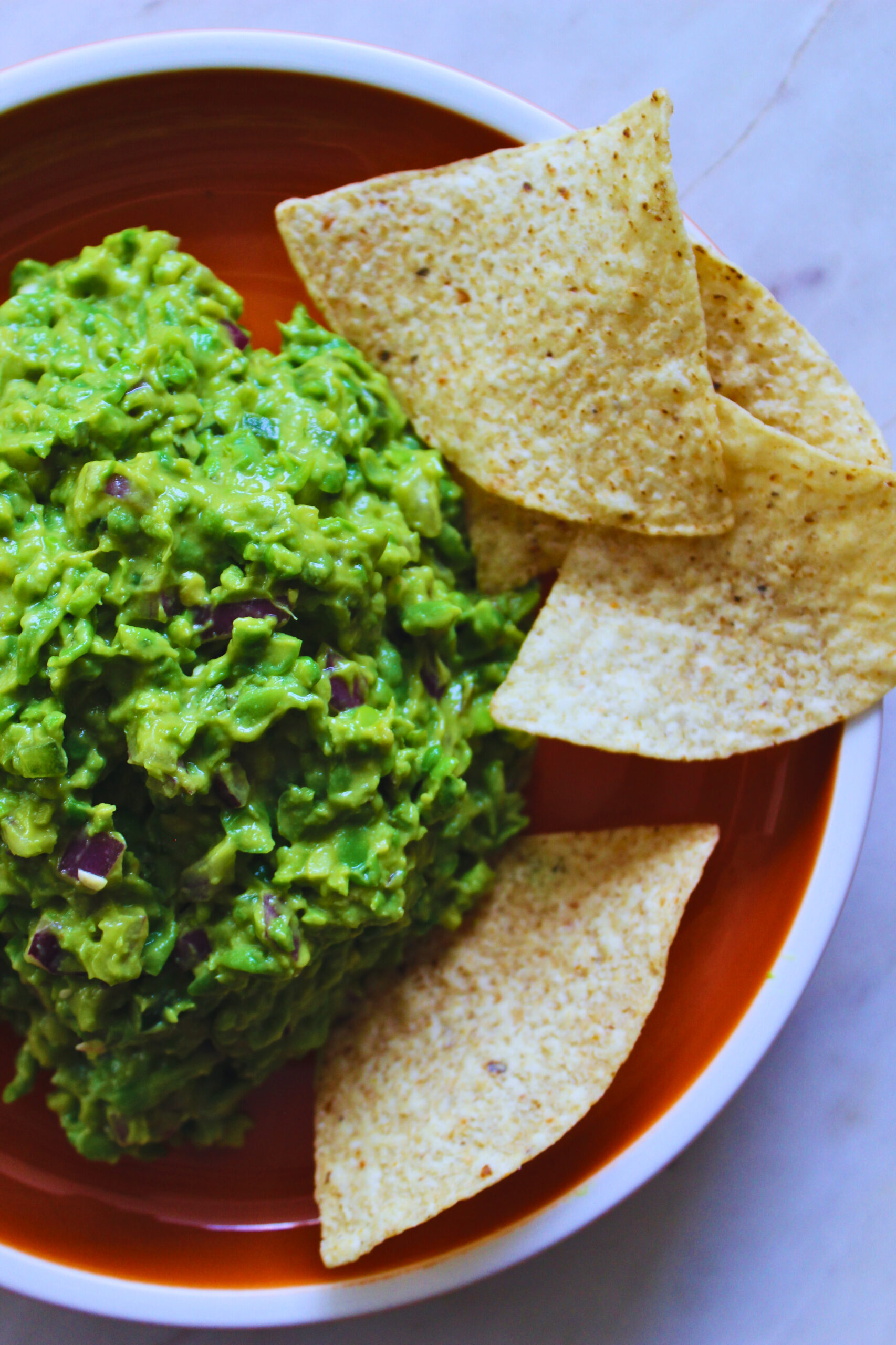 image of green pea guacamole on an orange plate with corn tortilla chips