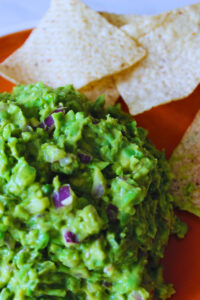 close up picture of green pea guacamole on an orange plate with chips