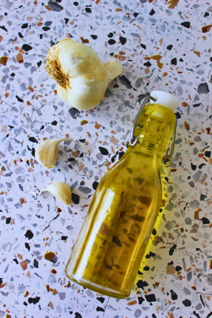 overhead image of fresh garlic and a glass bottle of garlic infused olive oil
