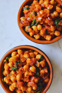 overhead image of two servings of chickpeas and spinach served in a Spanish ceramic tapa dish