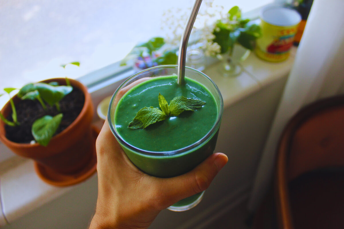 Image: Hand holding vibrant green smoothie garnished with mint.