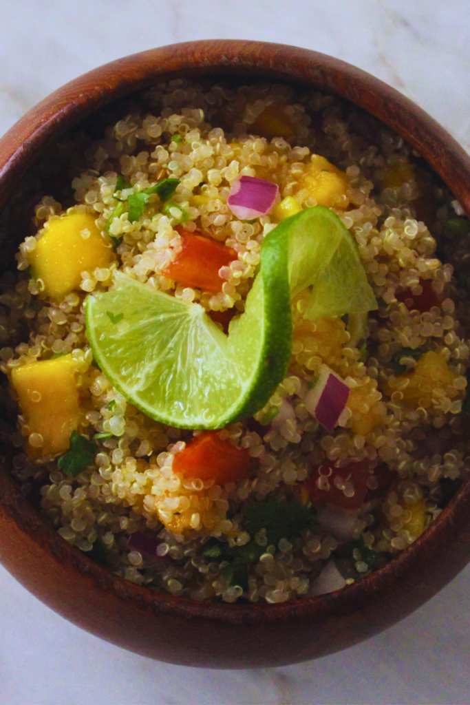 overhead image fo wooden bowl with quinoa mango salad topped with a lime twist