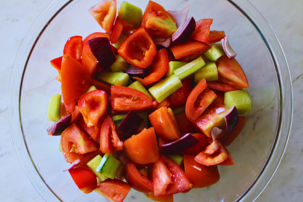overhead image of gazpacho ingredients chopped and mixed in a large clear bowl