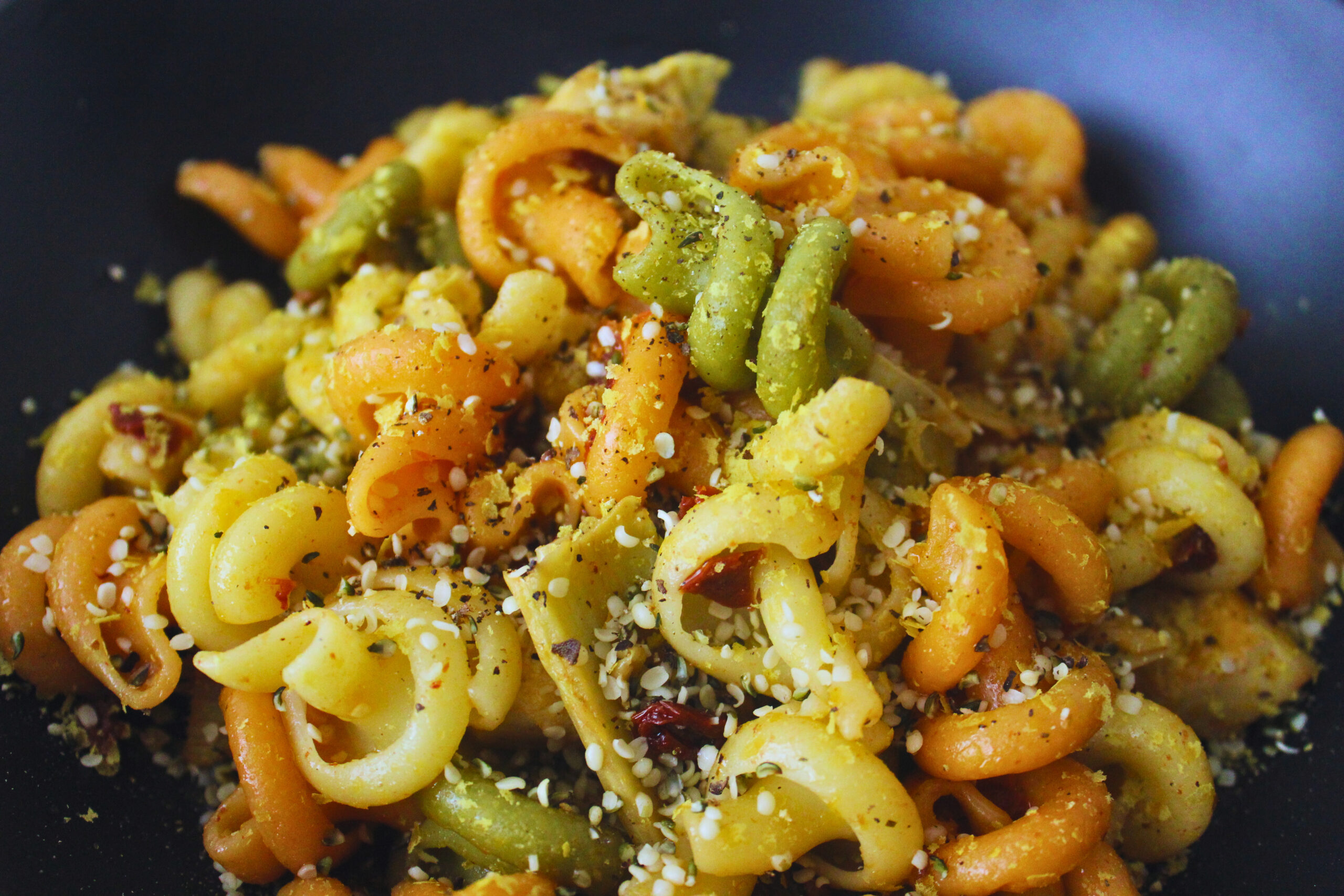 Close up image of lemon sundried tomato pasta with artichoke hearts, hemp seeds are sprinkled on it.