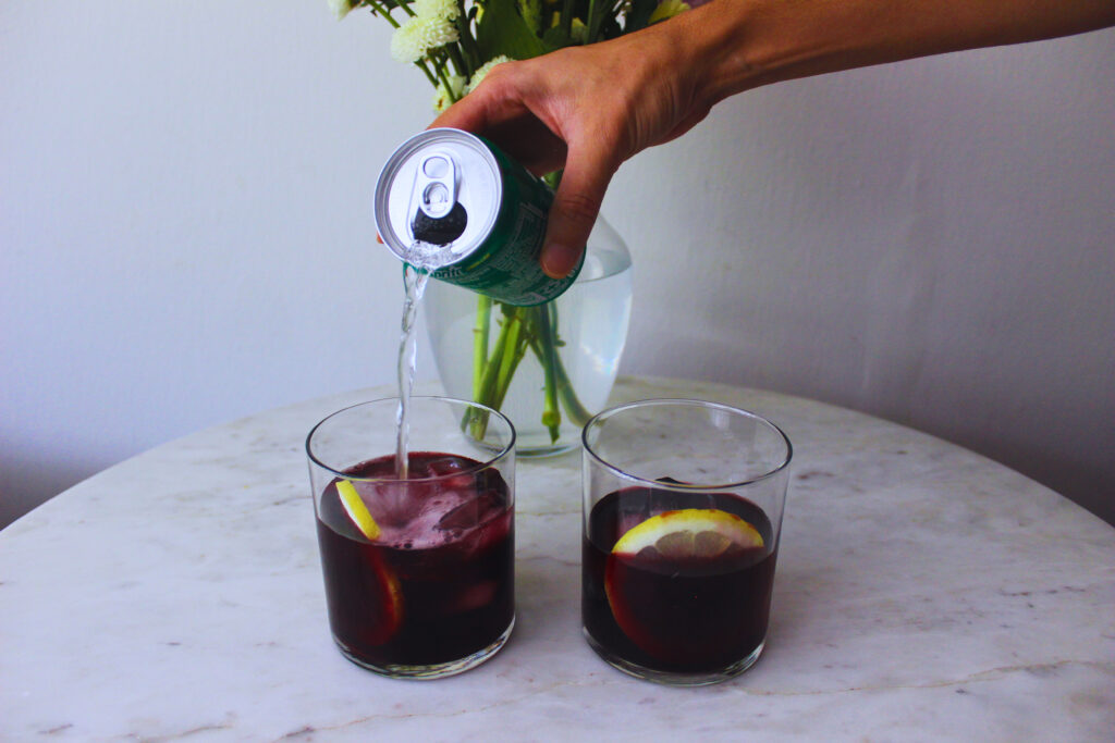 Image of lemon-lime soda being poured into two glasses with lemon wheel and red wine