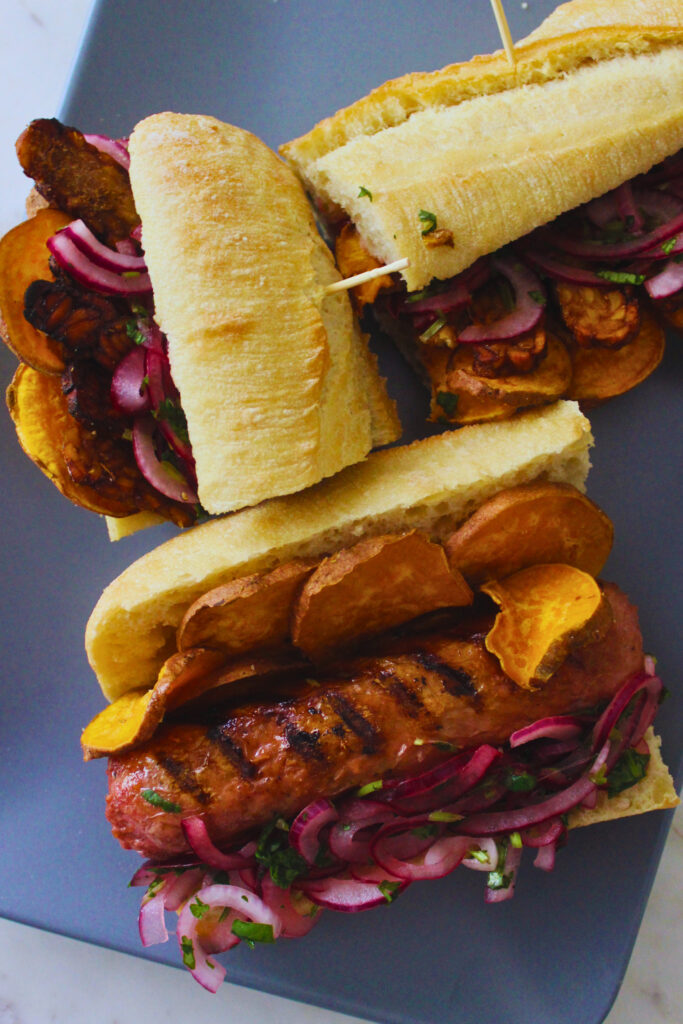 image of a plate fo sandwiches with vegan sausage or tempeh, sliced sweet potato and salsa criolla
