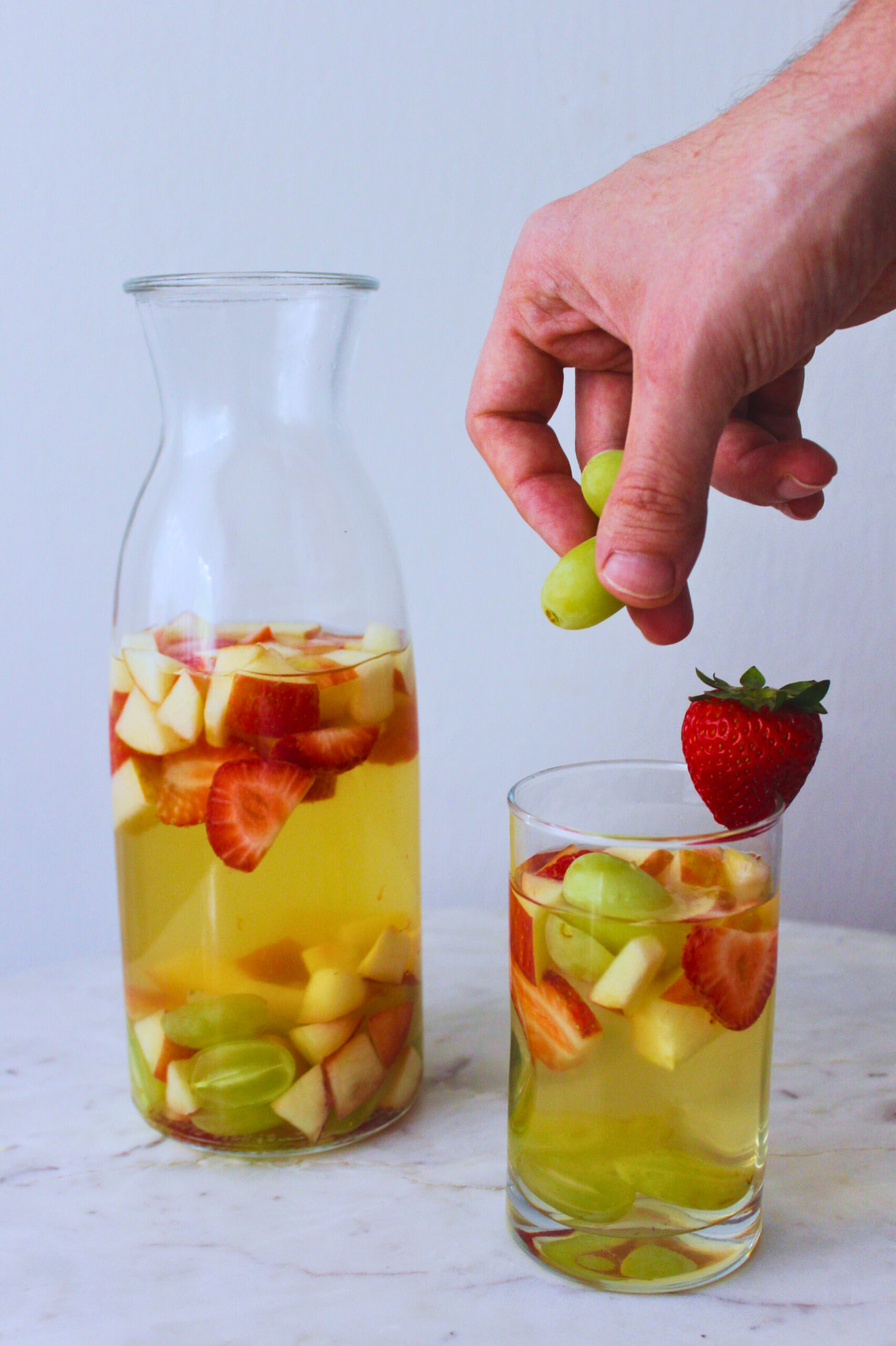 image of a carafe of sangria with a glass filled next to it and a hand adding frozen grapes to the glass