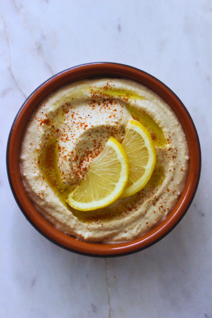 Overhead image of lemon garlic hummus, sprinkled with paprika, drizzled with olive oil and garnished with the lemon wedges thinly sliced