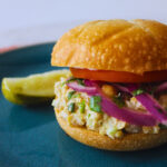 chickpea tuna sandwich with tomato and onion and a side pickle