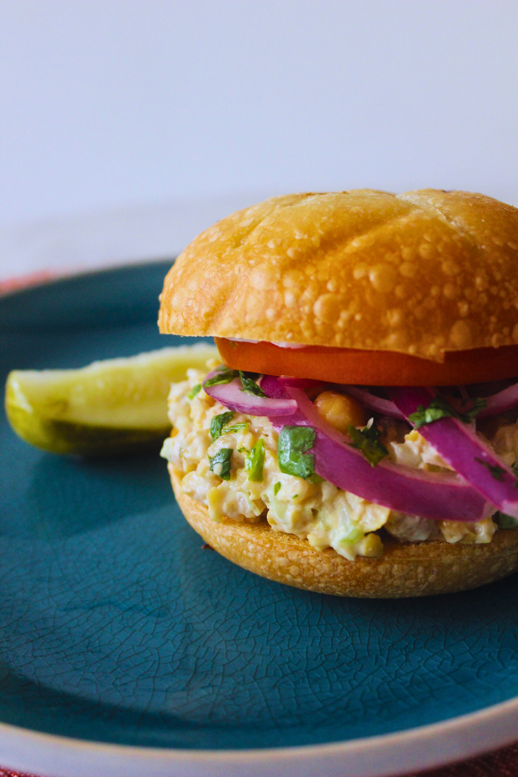 chickpea tuna sandwich with tomato and onion and a side pickle