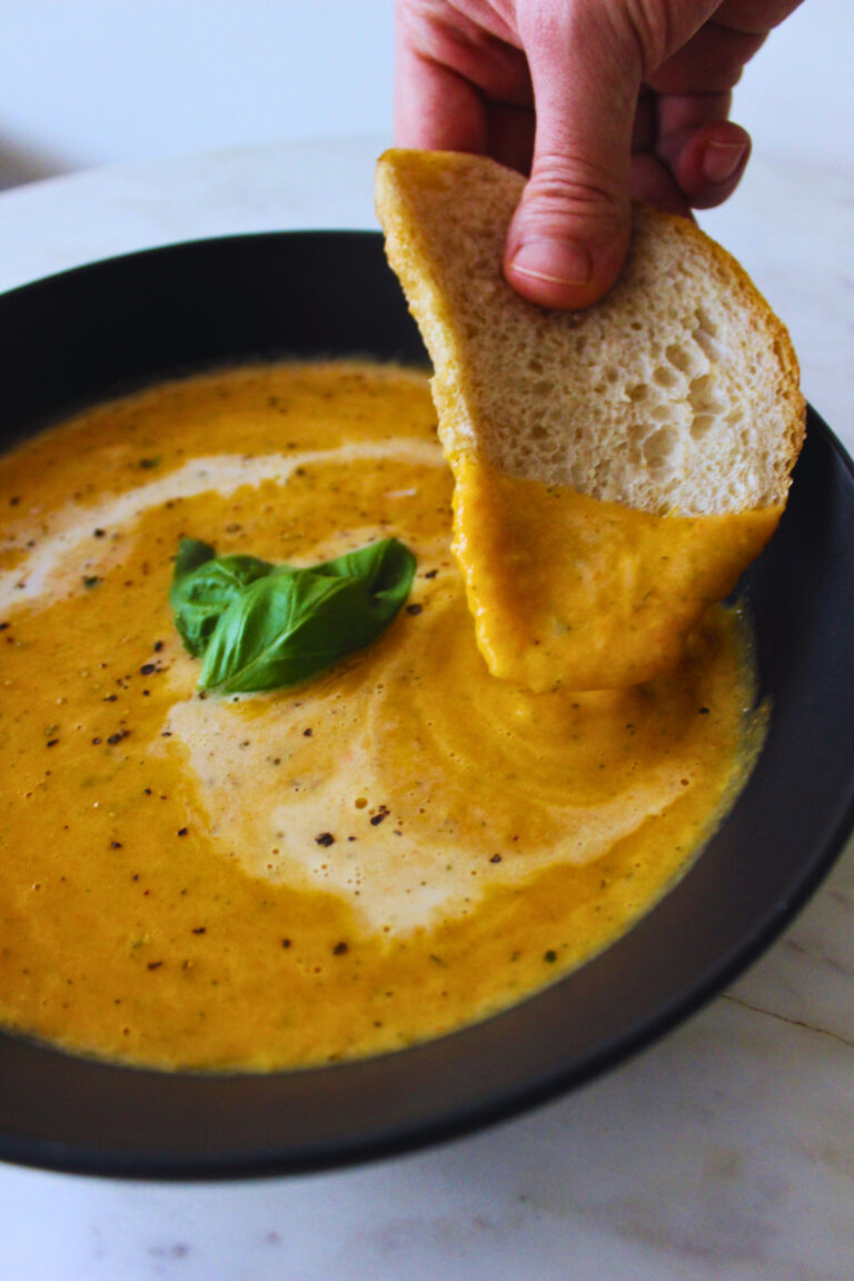 image of a a hand dipping bread into a creamy bowl of veggie soup