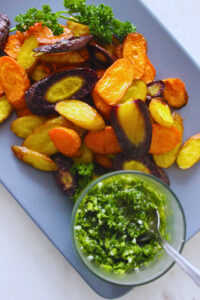 overhead image of roasted rainbow carrots with a side of fresh parsley sauce