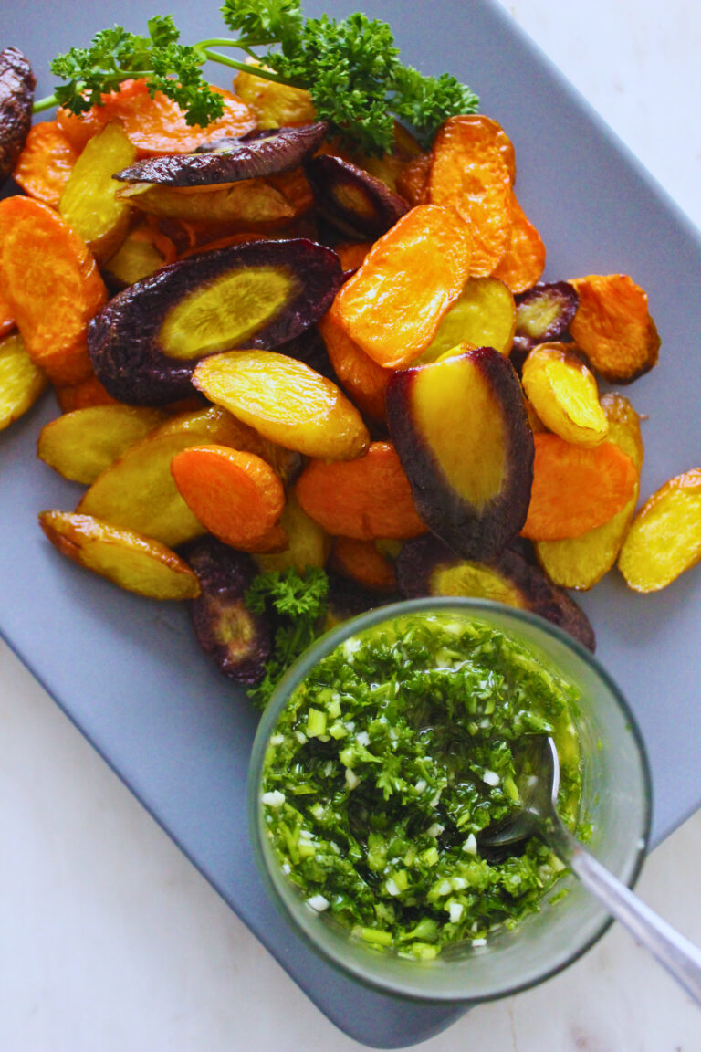 overhead image of roasted rainbow carrots with a side of fresh parsley sauce