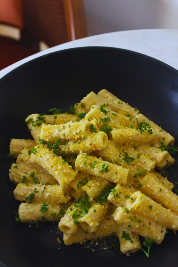 image of creamy cheesy vegan pasta plated and topped with parsley and nutritional yeast flakes