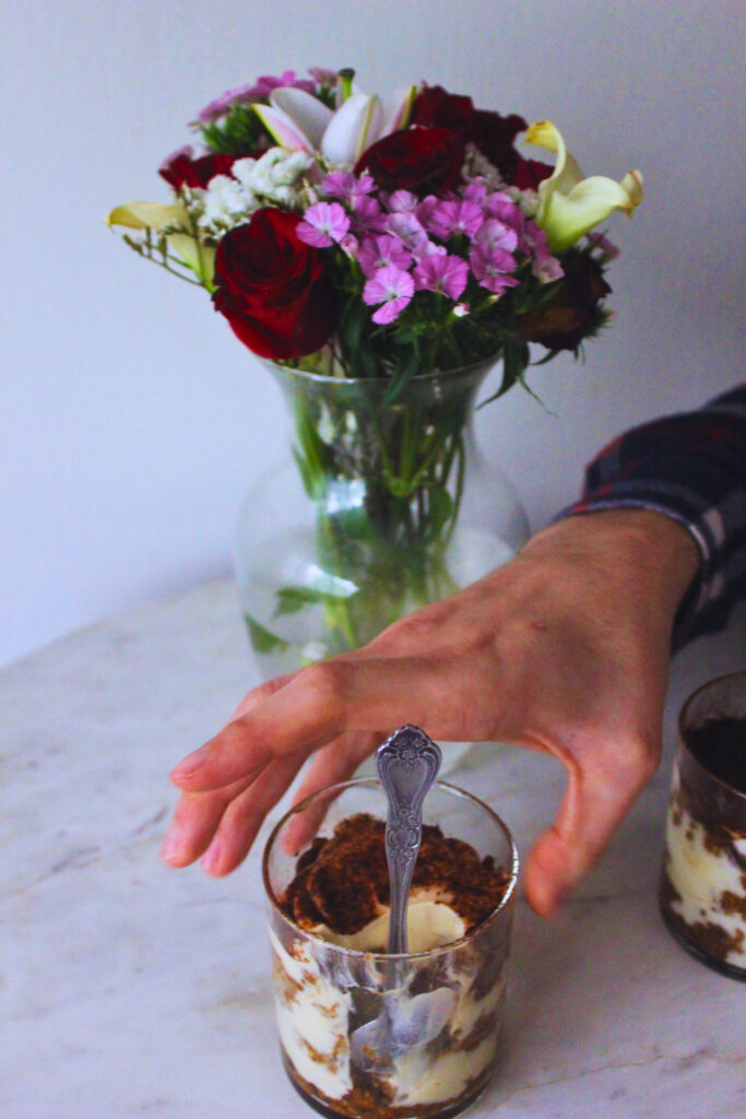 image of a hand reaching for a vegan tiramisu cup on a marble top table with a vase of flowers