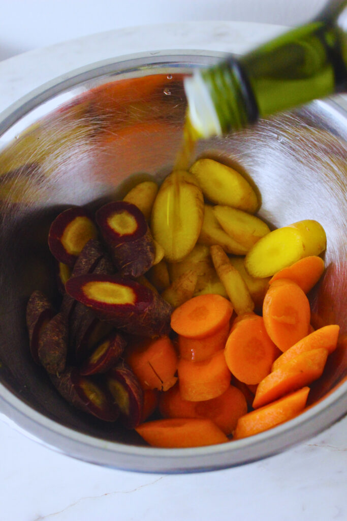 EVOO being poured over sliced rainbow carrots in a mixing bowl 