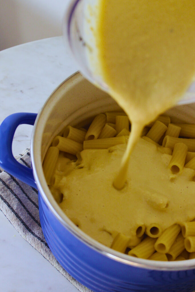 image of white bean cashew pasta sauce being poured into large pot with pasta