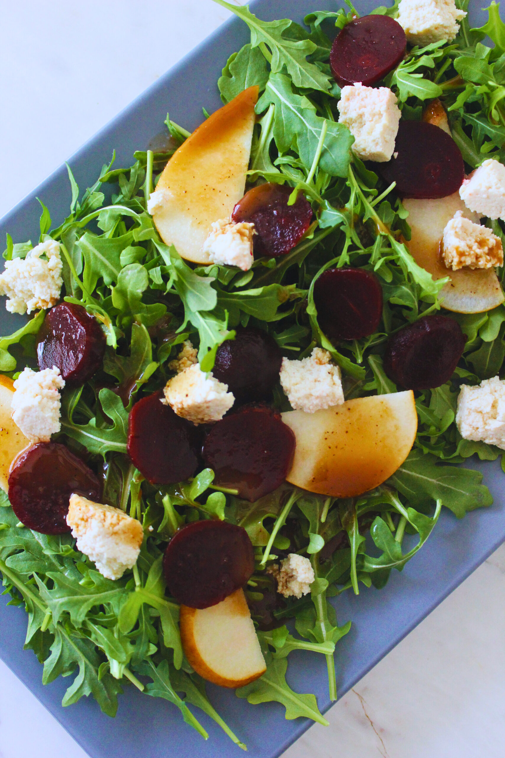 overhead image of a prepared arugula beet salad with tofu feta and pear, topped with balsamic vinaigrette.