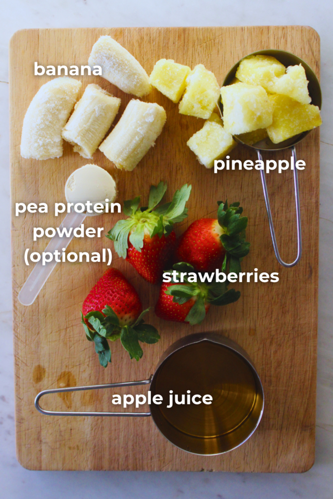 overhead image of all the fresh ingredients to make a strawberry banana pineapple smoothie on a wooden cutting board