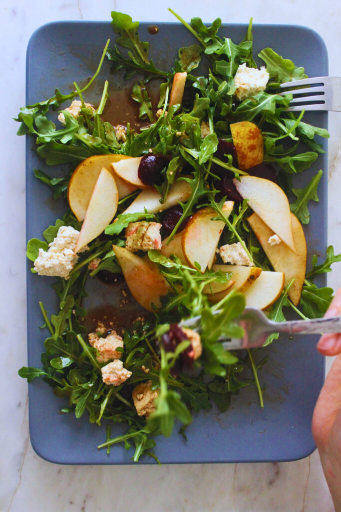 overhead image of a hand holding a fork enjoying a prepared arugula beet salad 