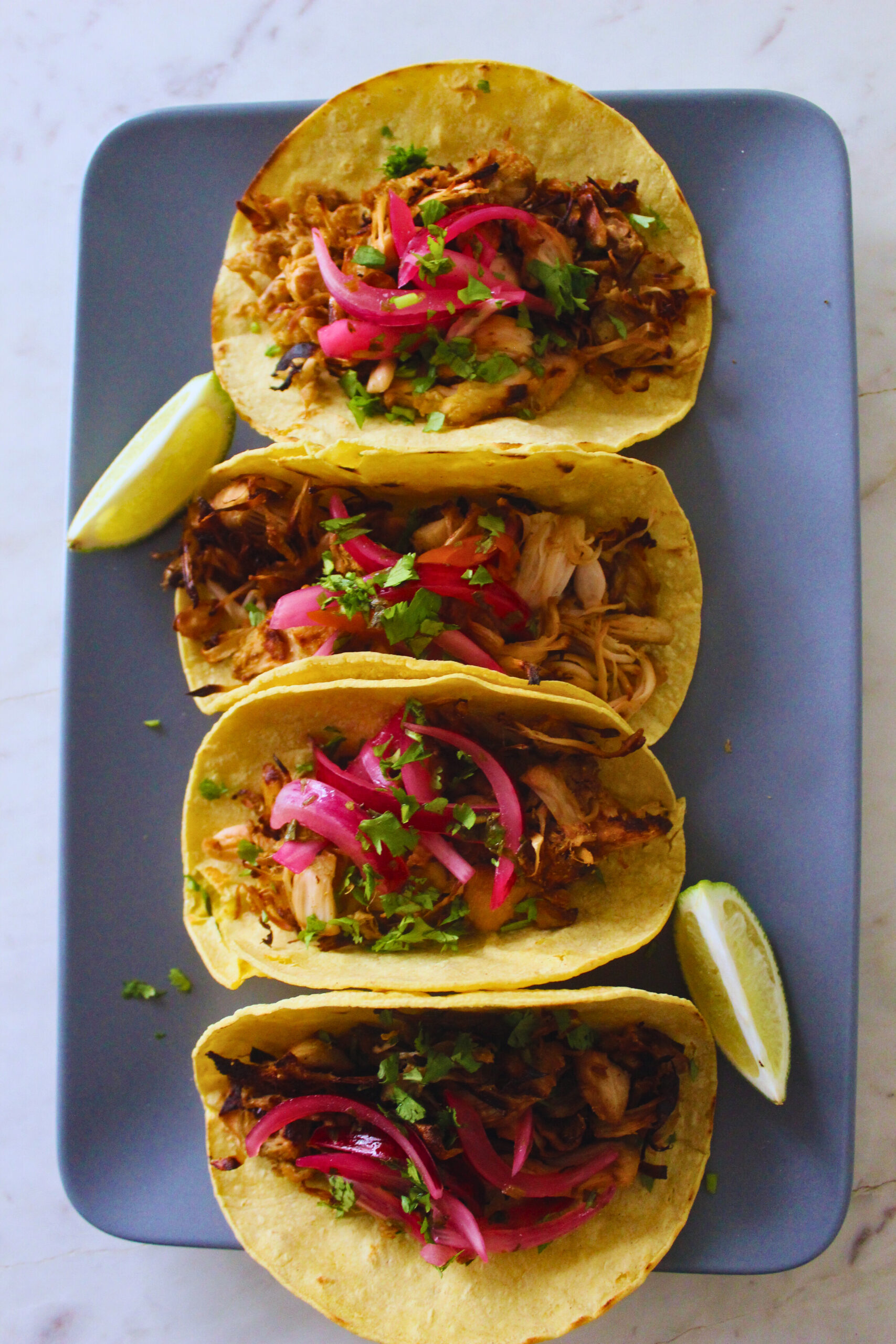 overhead image of four jackfruit carnita corn tacos topped with salsa criolla and cilantro