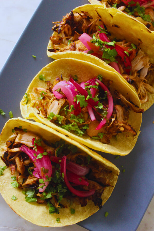 overhead image of a roll of jackfruit carnita tacos topped with red onion, lime and cilantro