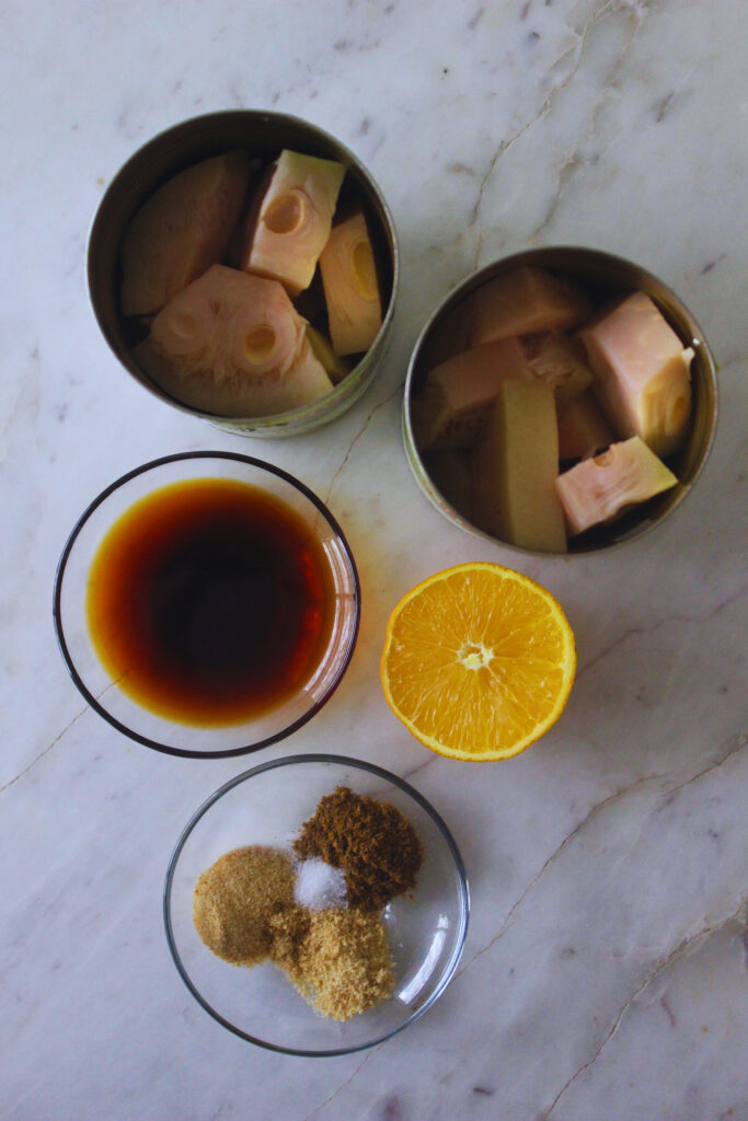 overhead image of two opened cans of jackfruit, a sliced orange, soy sauce and spices on a marble top