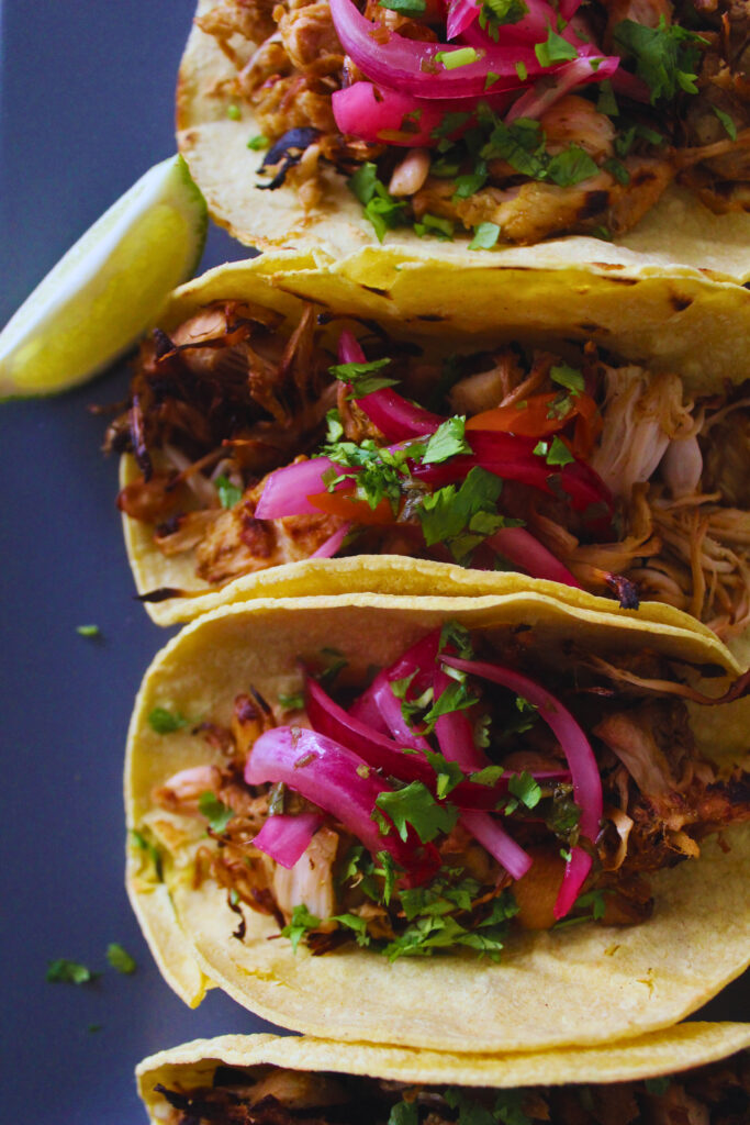 image of jackfruit carnitas tacos topped with red onion, cilanto, and lime