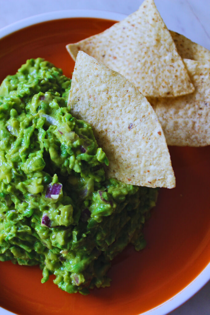 image of green pea guacamole on an orange plate with tortilla chips