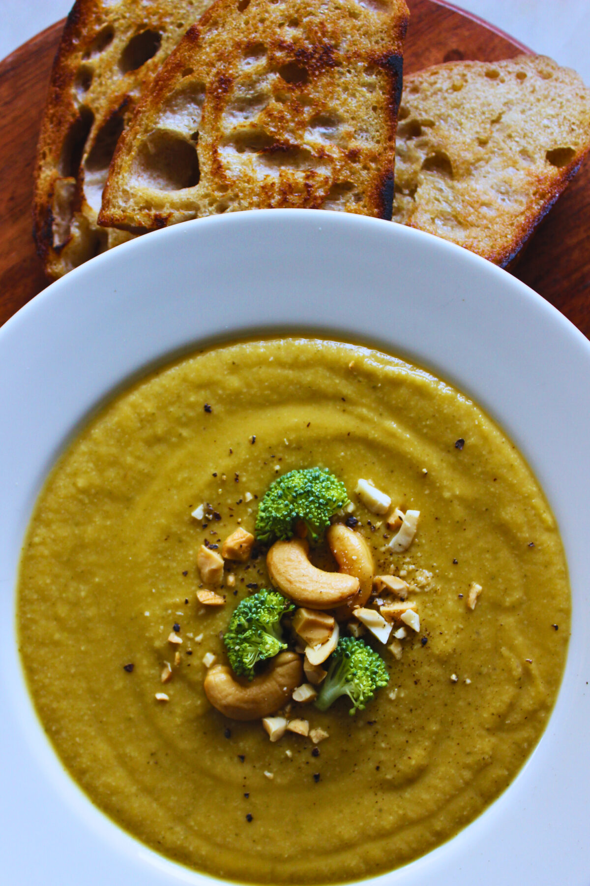 Creamy sweet potato broccoli soup served with a side of toasted sourdough bread and topped with chopped cashews and broccoli