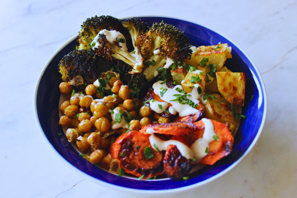 vibrant bowl of roasted carrots, chickpeas, potatoes, and broccoli topped with lemon tahini dressing and chopped parsley