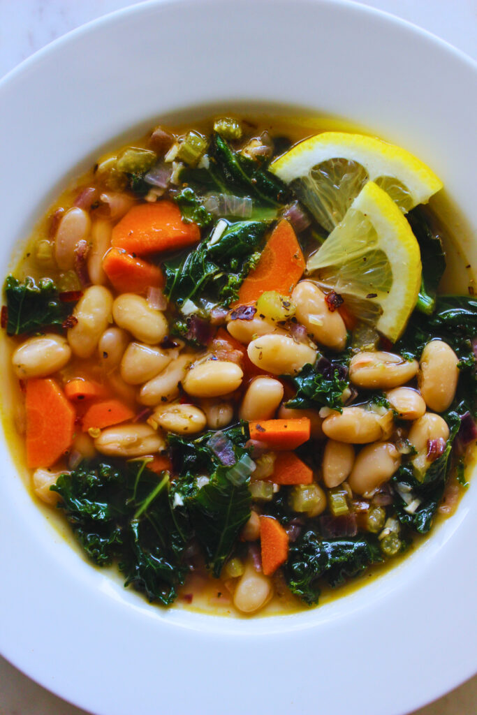 overhead image of lemon white bean kale soup topped with lemon slices and red pepper flakes