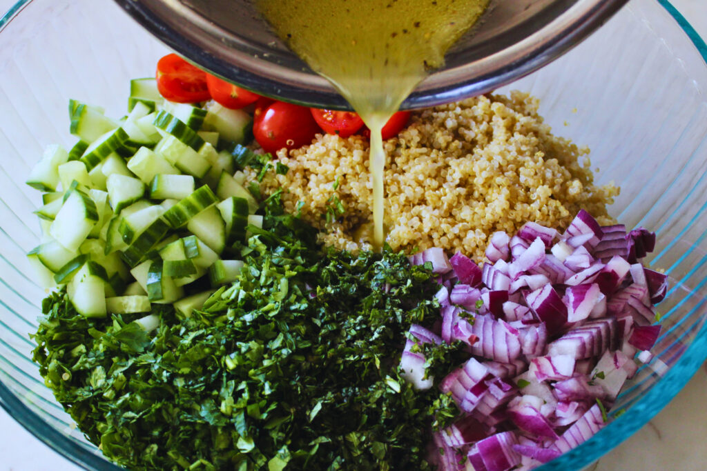 image of quinoa tabbouleh salad in a large glass bowl with dressing being poured