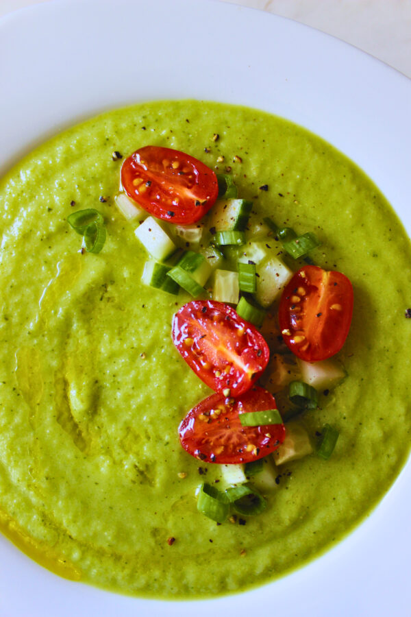 overhead image of green zucchini gazpacho topped with fresh tomatoes, cucumber and green onion.